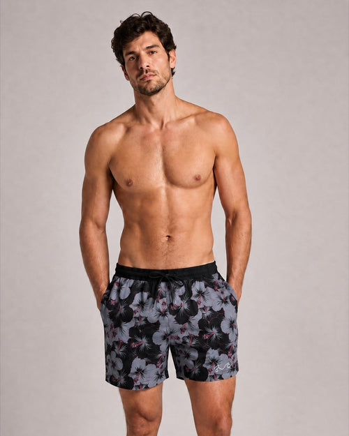 A shirtless man modeling patterned swim trunks against a plain light gray studio background.