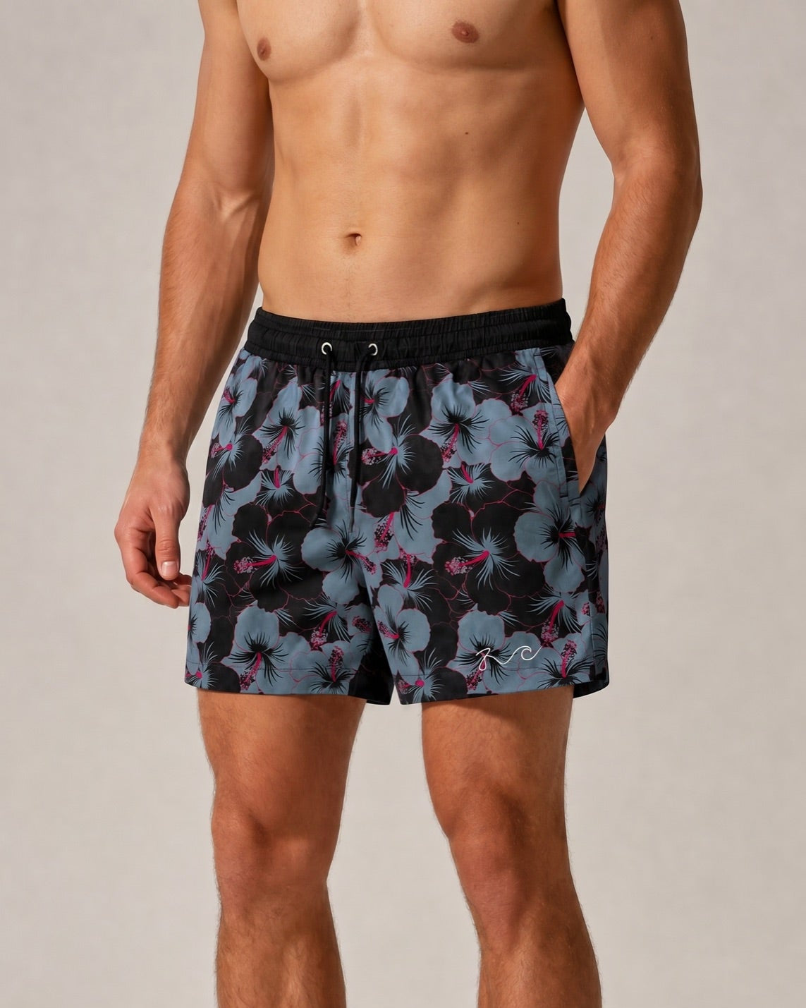 A man wearing patterned swim trunks with a black waistband and a blue, black, and pink floral print, shown from the chest down against a light gray studio background.