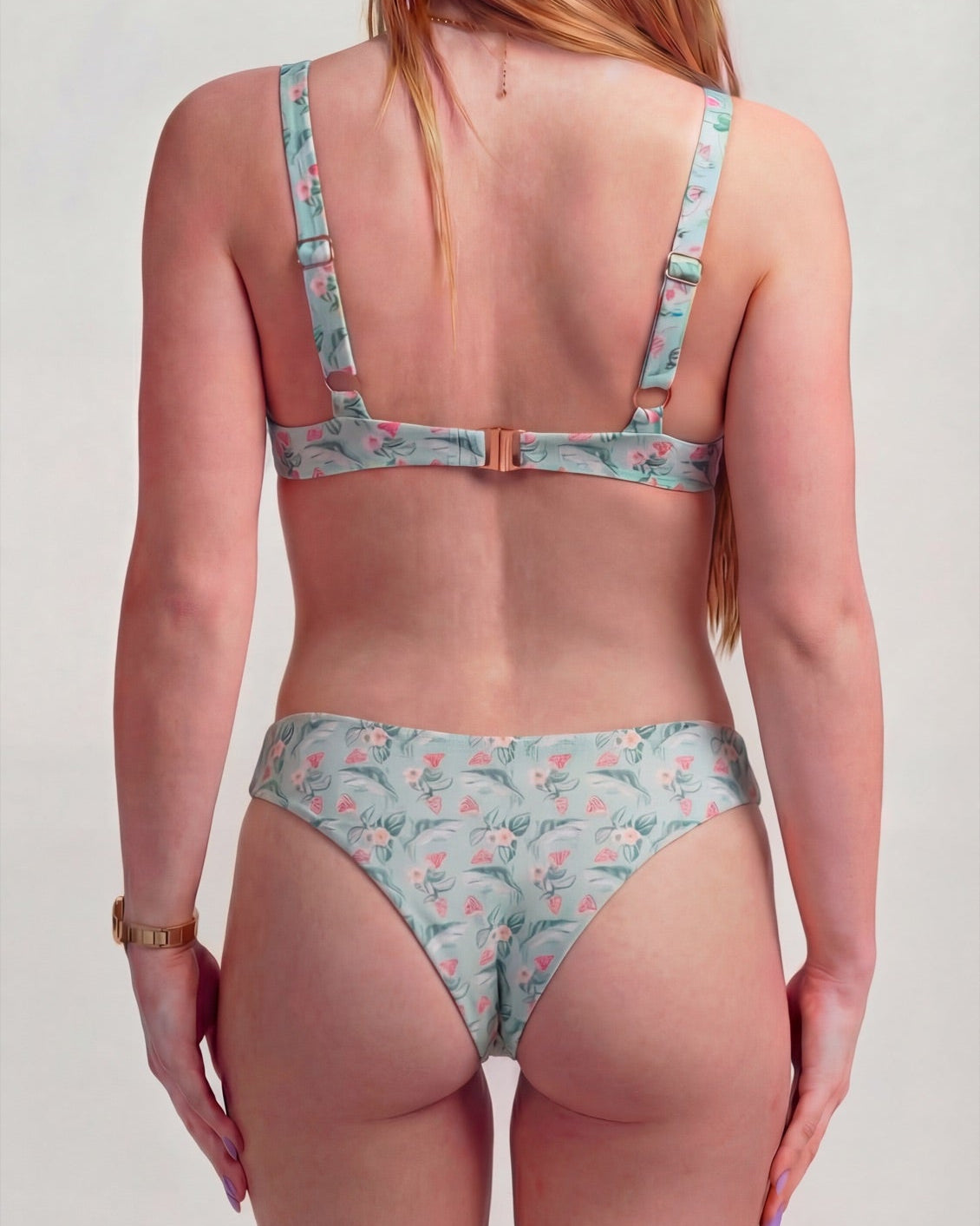 A woman shown from the back wearing a two-piece bikini with a light blue and pink flamingo pattern, set against a plain light gray background.