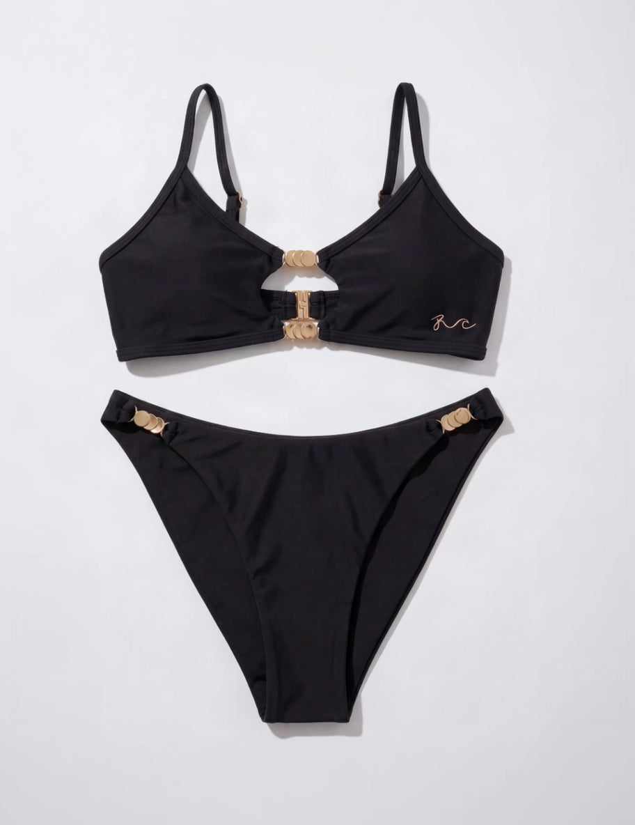 A two-piece black bikini set with gold-tone decorative hardware. The bikini top features a center cutout framed by gold rings, and the matching bottoms have gold rings at the hip.