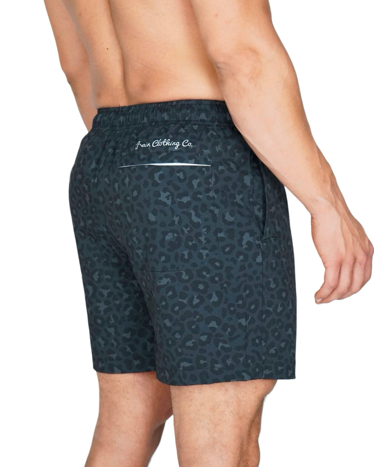 Rear view of a man wearing dark teal and black leopard-print swim trunks with 'Fusion Clothing Co.' printed in white on the back waistband, against a plain white background.