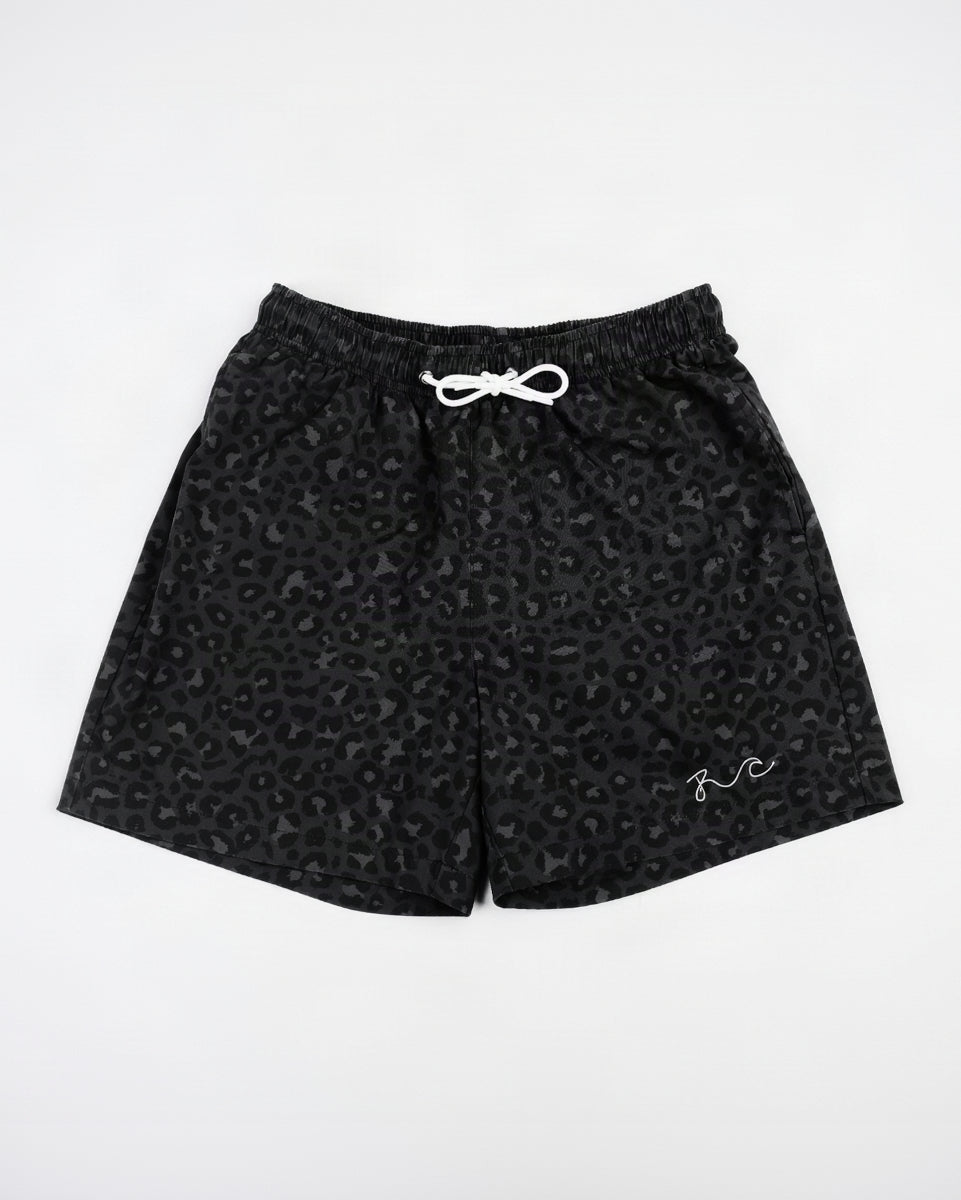 Black leopard print swim shorts with a white drawstring and a small white script logo on the lower left leg, displayed flat against a white background.
