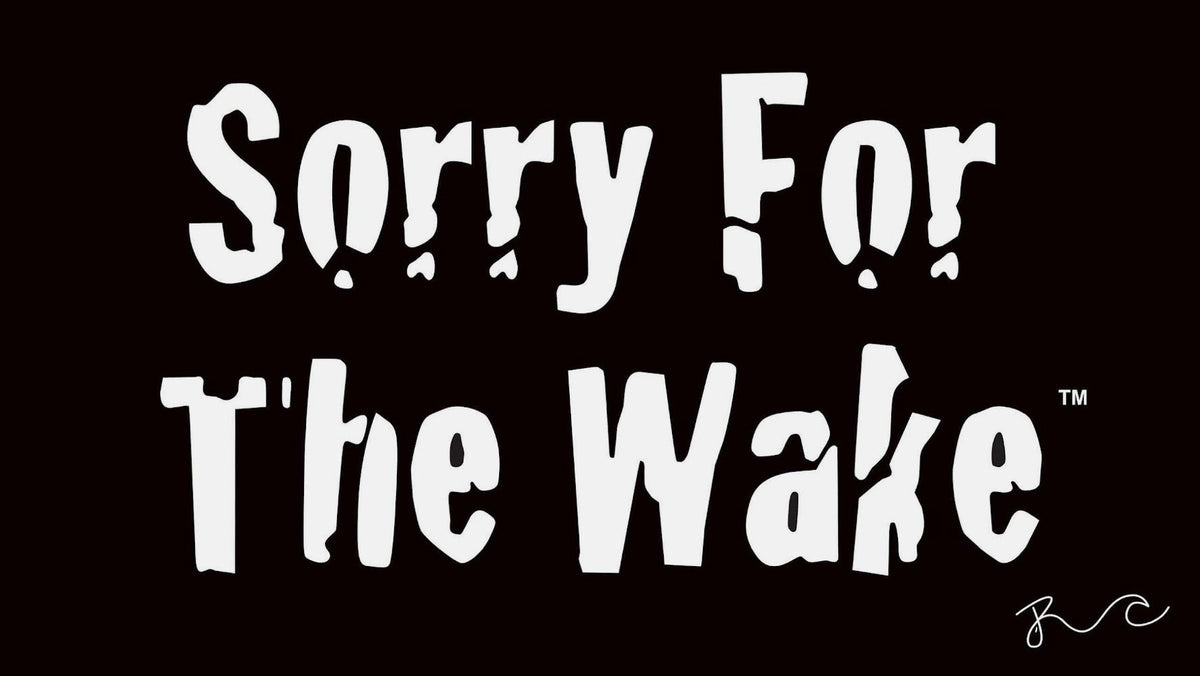 A black flag or banner with the phrase 'Sorry For The Wake' printed in large white stylized lettering. A white hanging edge with grommets is visible along the left side, and a small white script mark appears in the lower right corner.